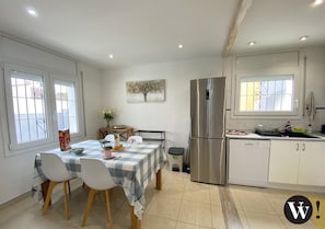 A modern kitchen with a stainless steel refrigerator, a dishwasher, and a dining area with a checkered tablecloth and white chairs. - Villa 3 bedrooms, 2 bathrooms, private pool, air conditioning and wifi (L'Escala)