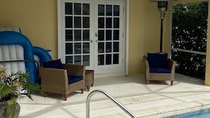 Un espace aménagé au bord de la piscine, avec des fauteuils en osier, une plante en pot et une porte à panneaux de verre.