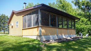 Una cabana de fusta amb un porxo gran i mosquiteres, envoltada d'un pati herbós i arbres.
