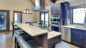 Une cuisine moderne dotée d’un îlot central, de fours encastrés et d’une grande fenêtre.