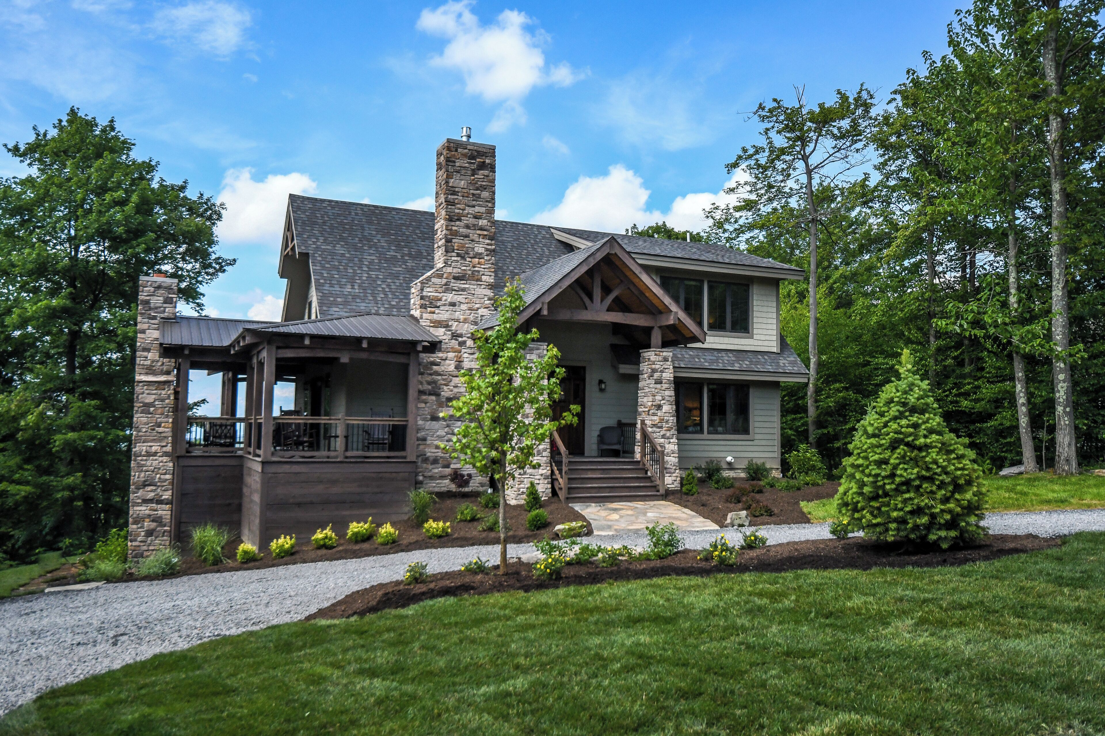 A two-story stone house with a stone chimney, a covered porch, and a well-maintained lawn.