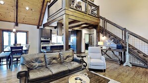 Un vaste espace de vie comprenant un canapé en cuir, un fauteuil blanc et une table basse en bois. Un escalier mène à un niveau supérieur doté d’un balcon.