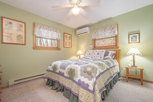 Quarto com uma cama grande, duas mesas de cabeceira com luminárias, um ventilador de teto e obras de arte botânicas emolduradas nas paredes.