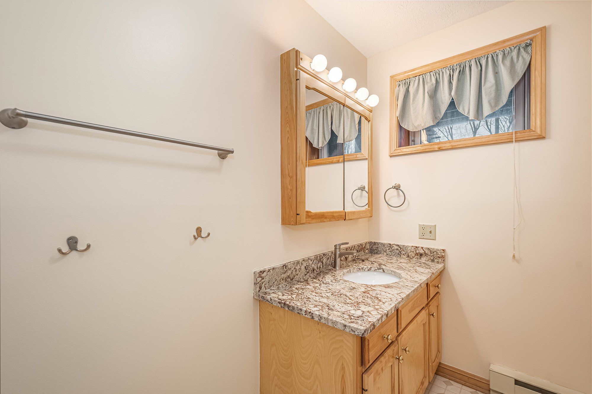 A bathroom with a vanity, a towel rack, a mirror with lights, and a window with curtains.
