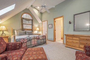 A bedroom with a sloped ceiling, a bed with patterned bedding, two bedside lamps, a wooden dresser, and a large mirror. - Adlerskron by Taylor Made Deep Creek (McHenry)