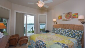 Un dormitorio con cama, ventilador de techo, vistas al exterior y obras de arte en la pared.