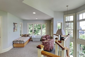 A bedroom with a bed, two chairs, a bench, a staircase, and large windows.
