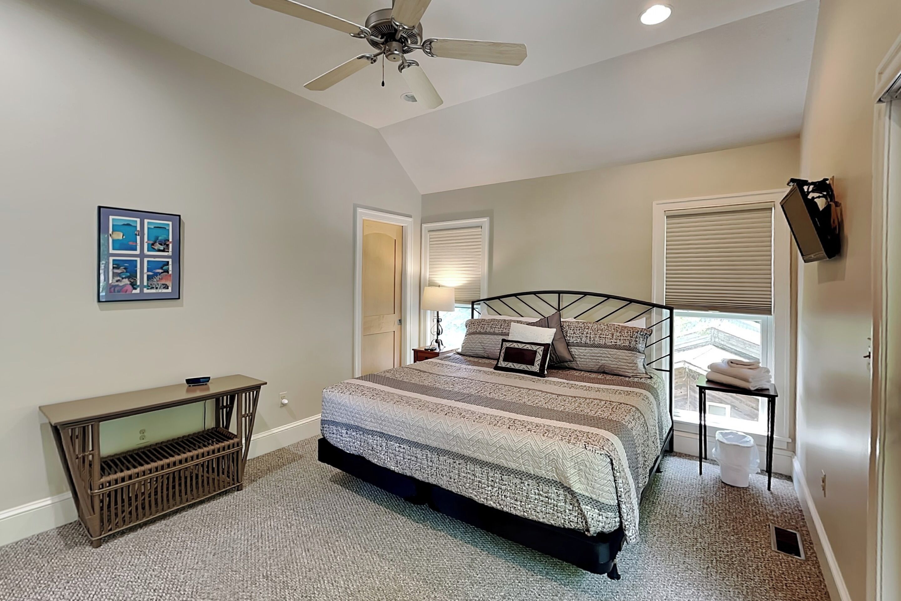 A bedroom with a bed, a ceiling fan, a nightstand, a lamp, and a picture on the wall.