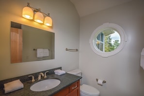 A bathroom with a sink, mirror, and toilet. There is a window with a view of trees.