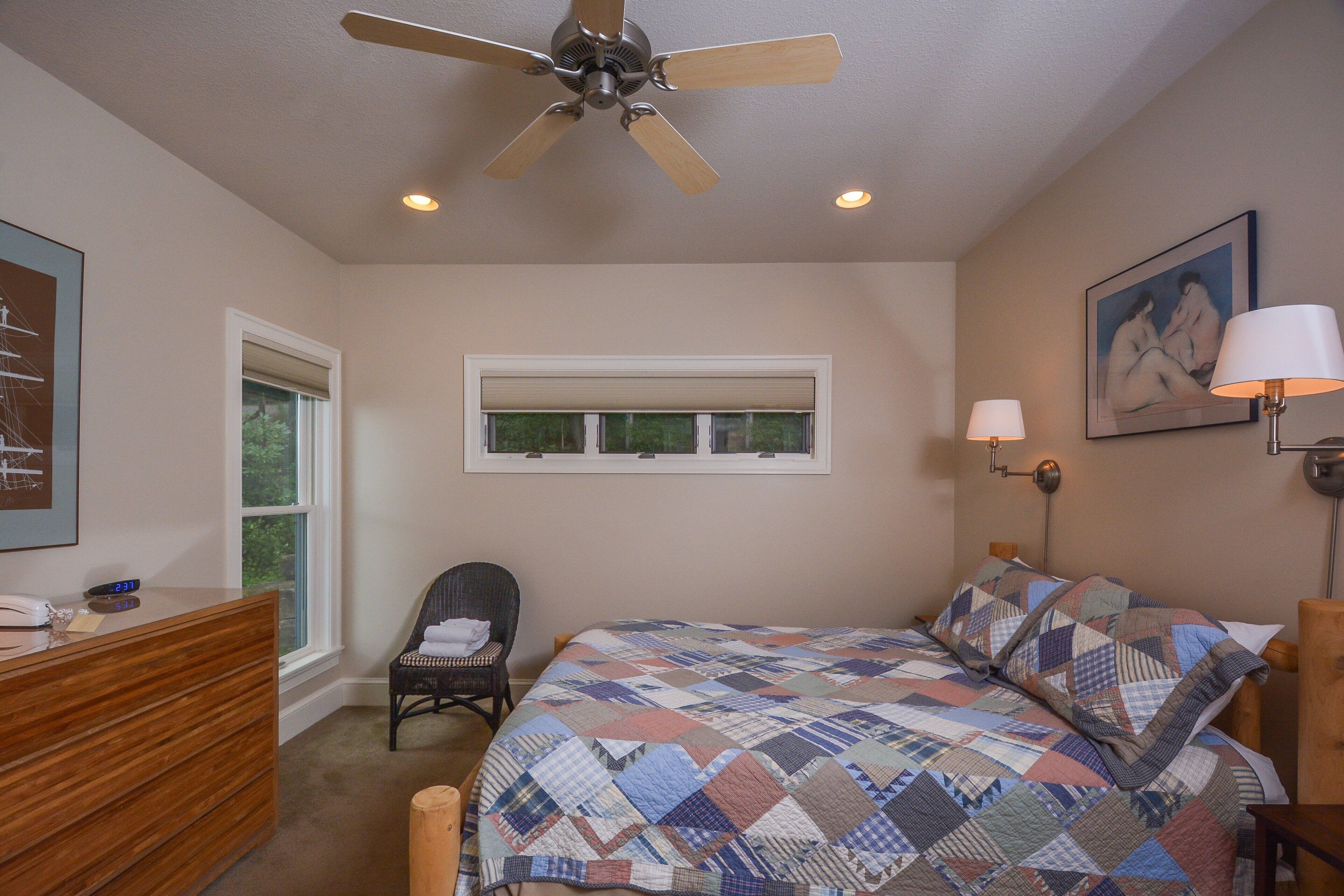 A bedroom with a bed, a chair, a dresser, a window, and a ceiling fan.