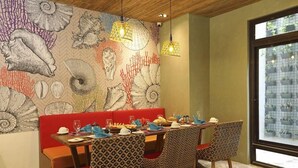 A dining area with a mural of seashells and coral, a red cushioned bench, patterned chairs, and hanging pendant lights. - Lagun Hotel (El Nido)
