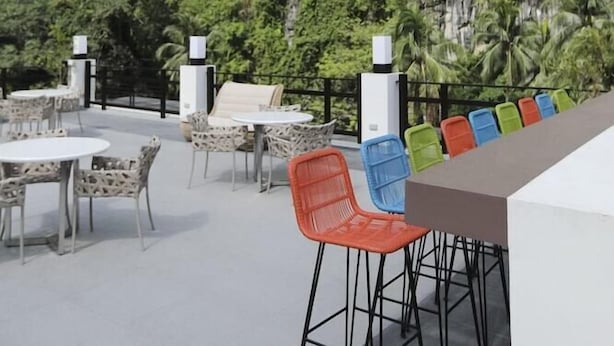 An outdoor seating area with tables and chairs, a bar, and a view of a lush green hillside. - Lagun Hotel (El Nido)