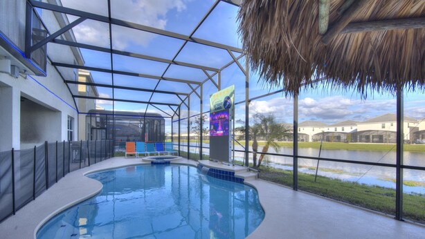 An indoor swimming pool with a glass ceiling, a thatched roof, and a view of a lake and buildings.
