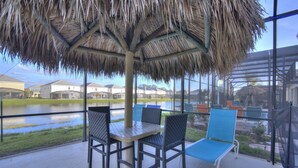 A covered outdoor seating area with a thatched roof, tables, and chairs.