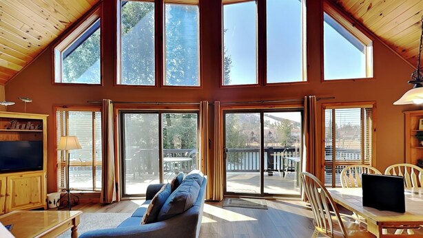 A spacious room with a high ceiling, large windows, a cozy seating area, and a dining table.