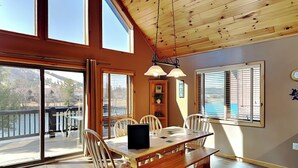 A dining area with a wooden table and chairs, large windows, and a view of a body of water.