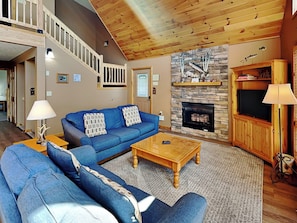 A living room with a blue sofa, wooden coffee table, fireplace, and a staircase. - Almost Paradise by Taylor Made Deep Creek (McHenry)