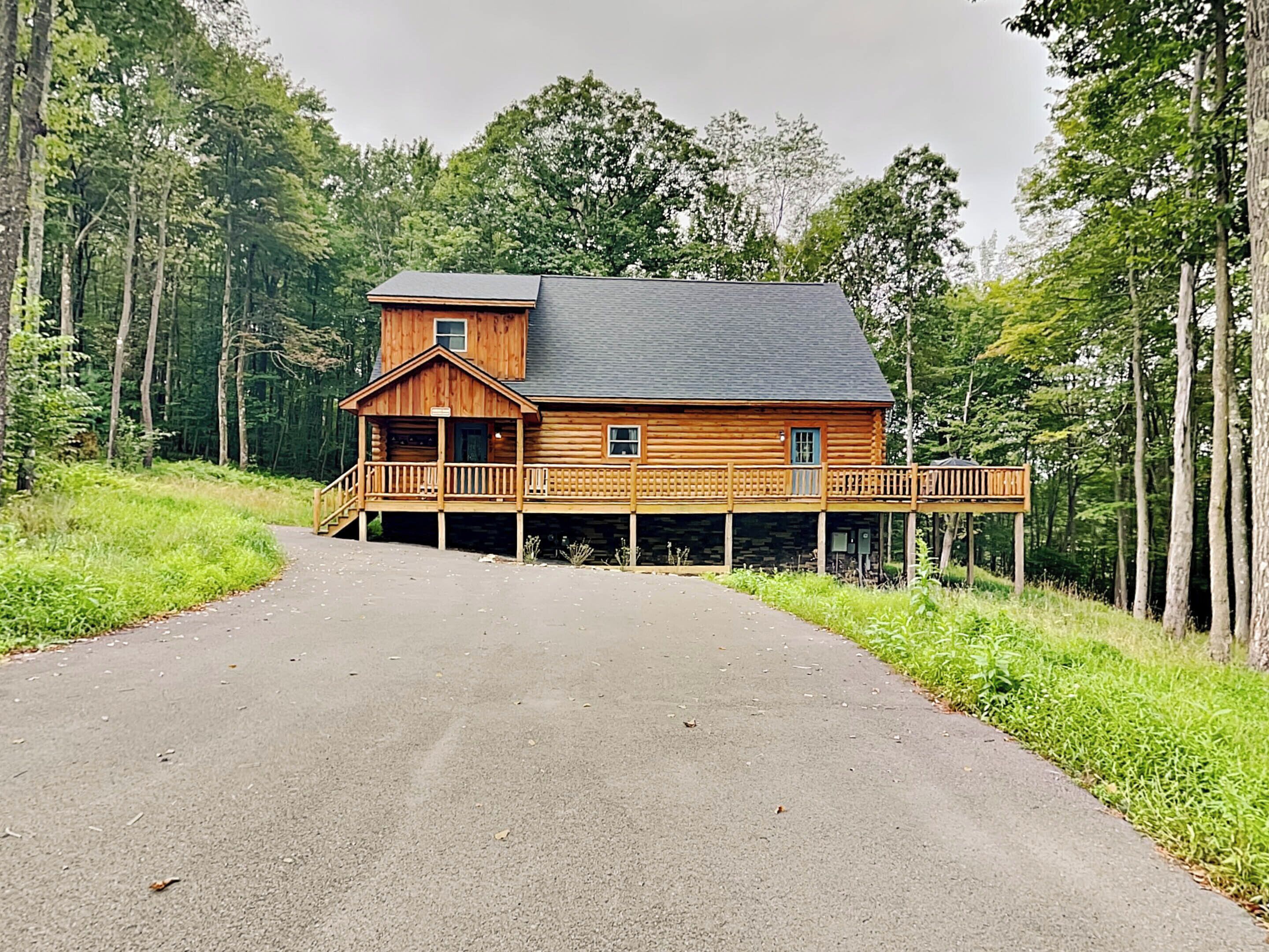Una cabaña de troncos con un porche y una terraza, rodeada de bosque.