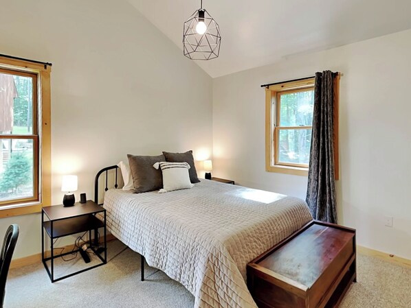 Een slaapkamer met een bed, nachtkastjes, een bureau en een hanglamp.