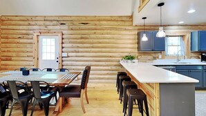 A log cabin interior with a dining area, kitchen, and bar seating. - Almost Eden by Taylor Made Deep Creek (McHenry)