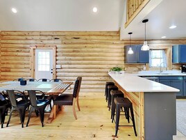 Interior de una cabaña de troncos con comedor, cocina y barra.