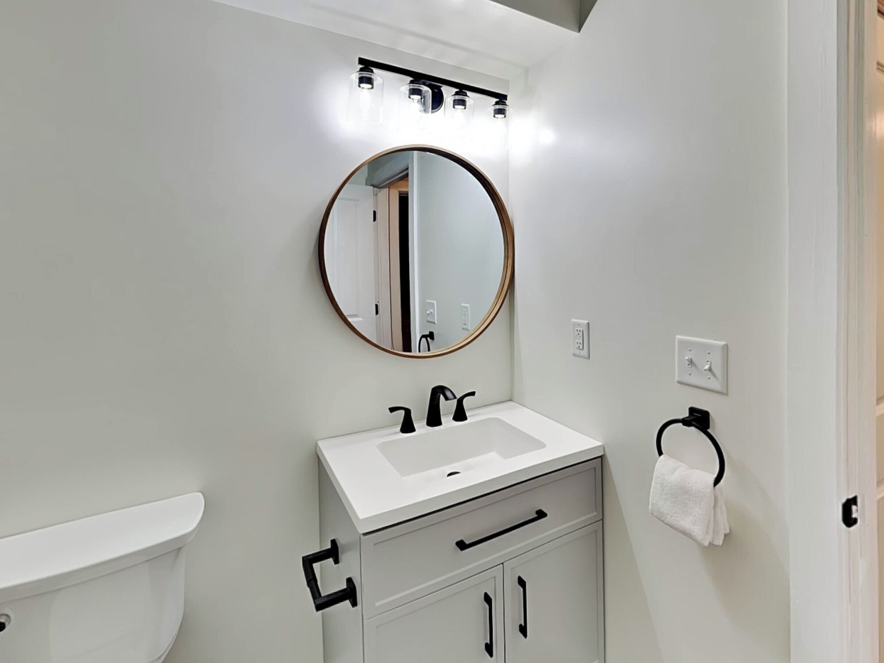 A modern bathroom with a white sink, a round mirror, and a toilet.