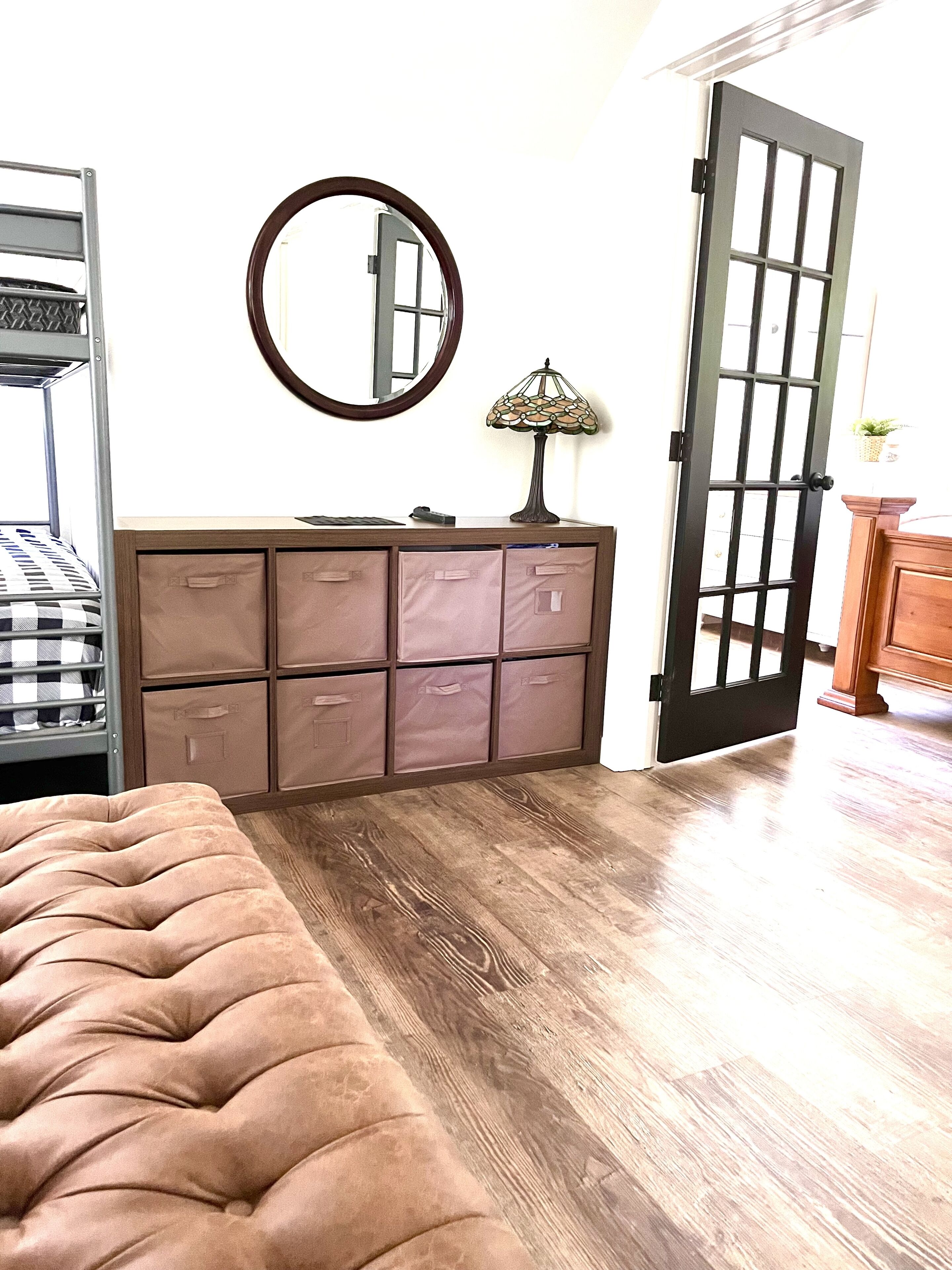 A bedroom with a bunk bed, a dresser with drawers, a mirror, and a door.