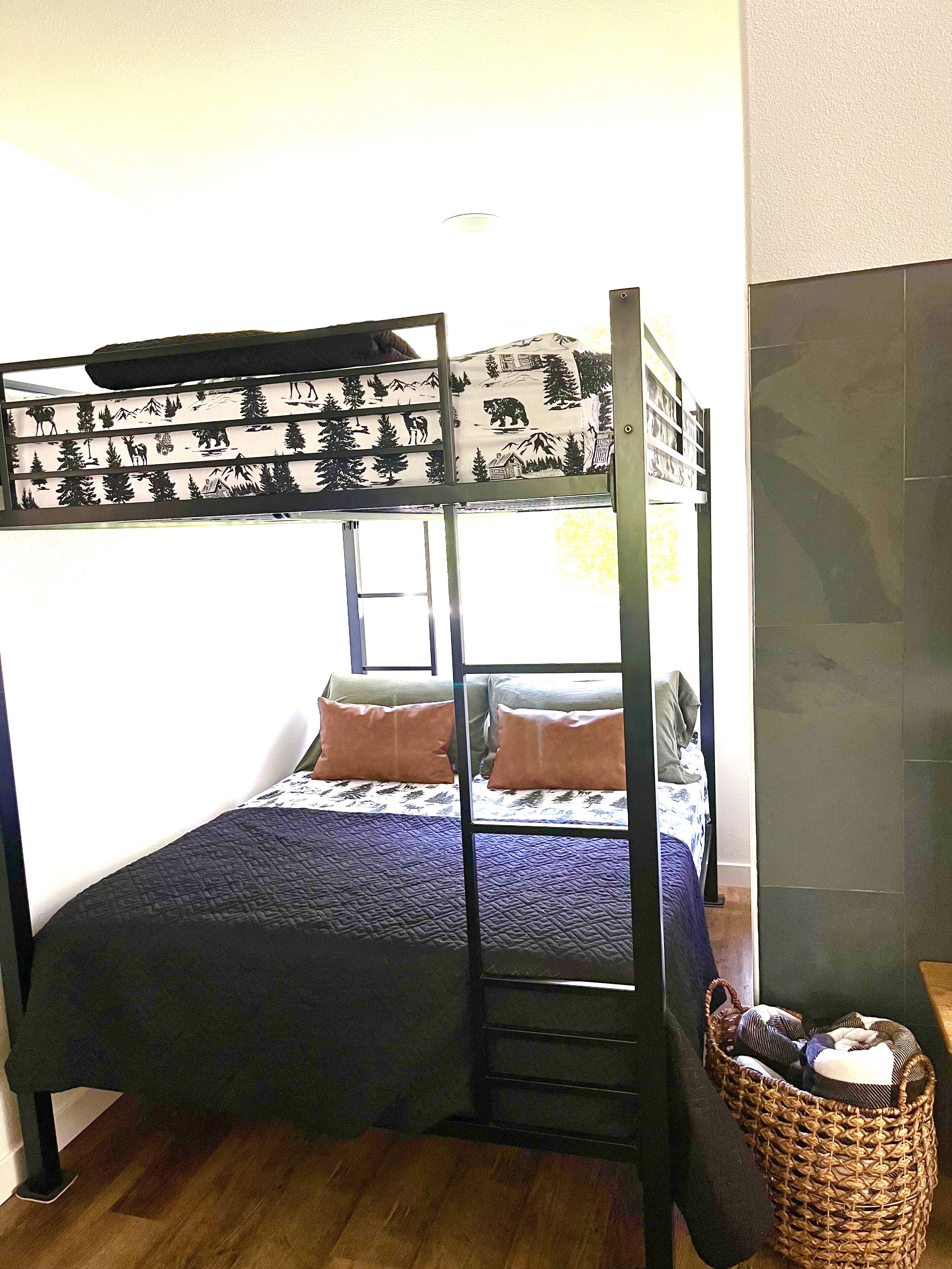 Una cama litera con escalera, una cesta tejida y una ventana que da a árboles y montañas.