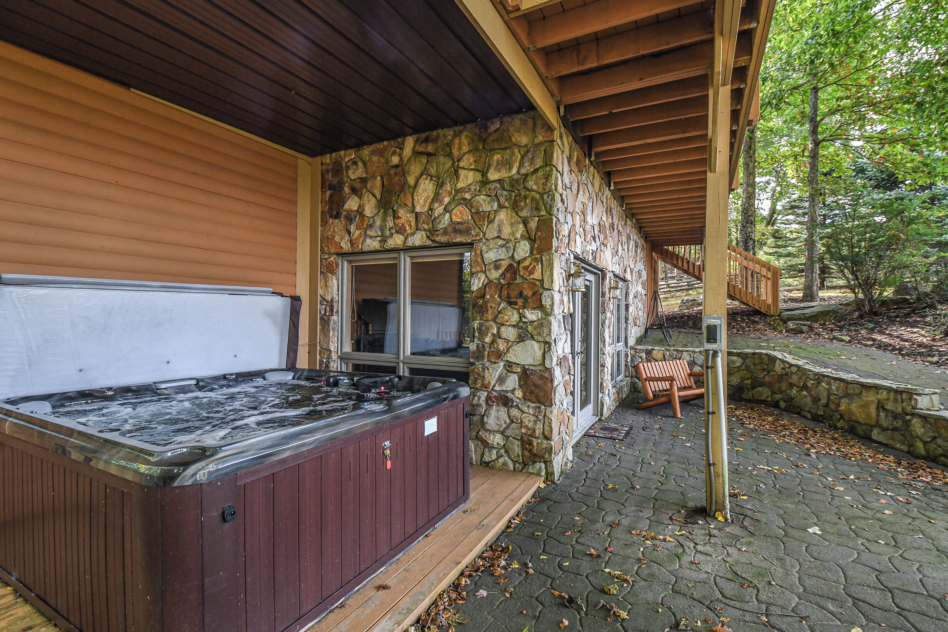 A stone exterior with a hot tub and wooden deck.