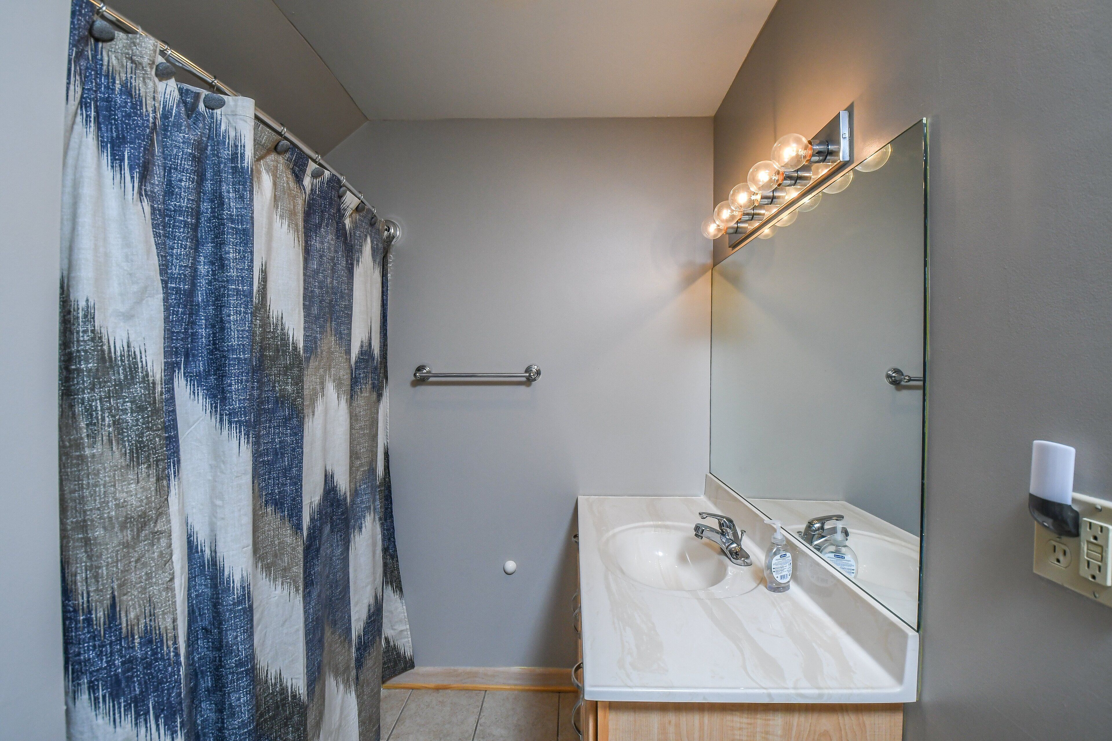 Une salle de bain avec un rideau de douche, un lavabo, un miroir et un luminaire.