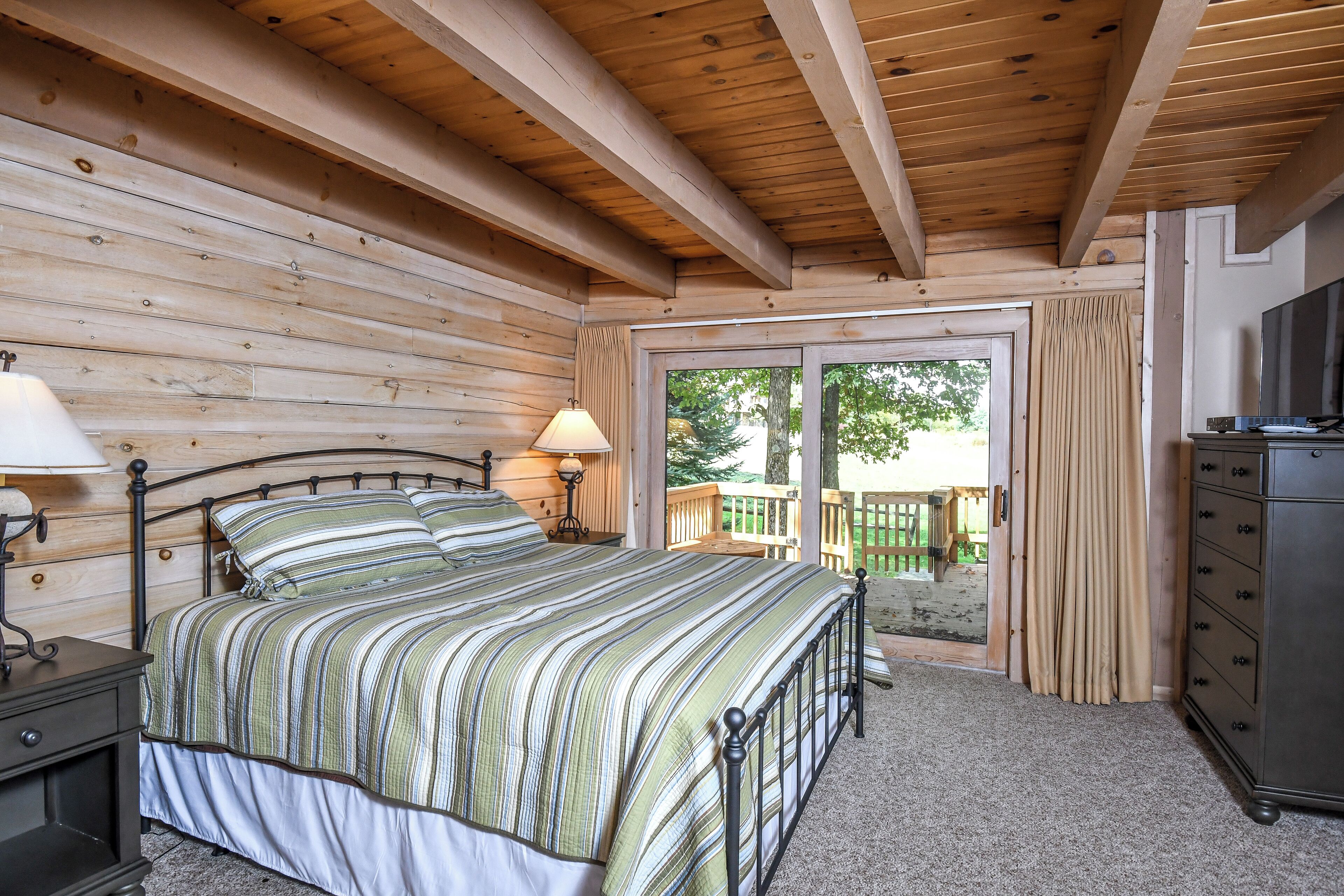 A wooden-paneled bedroom with a bed, nightstand, dresser, and a view through a glass door.