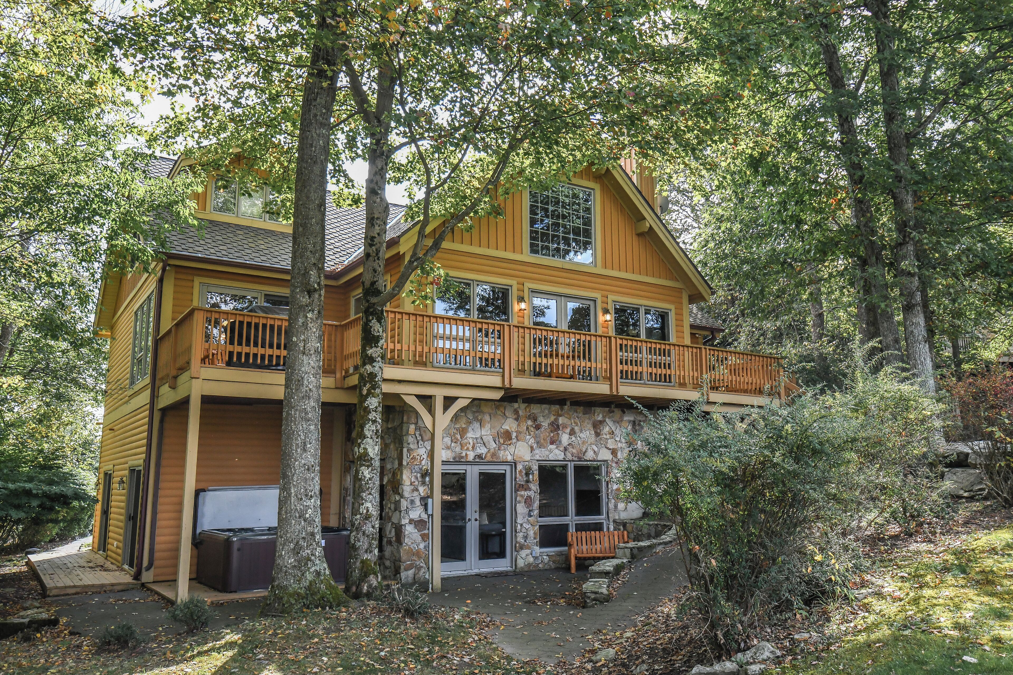 A two-story log cabin with a stone foundation, a balcony with wooden railings, and a stone fireplace.