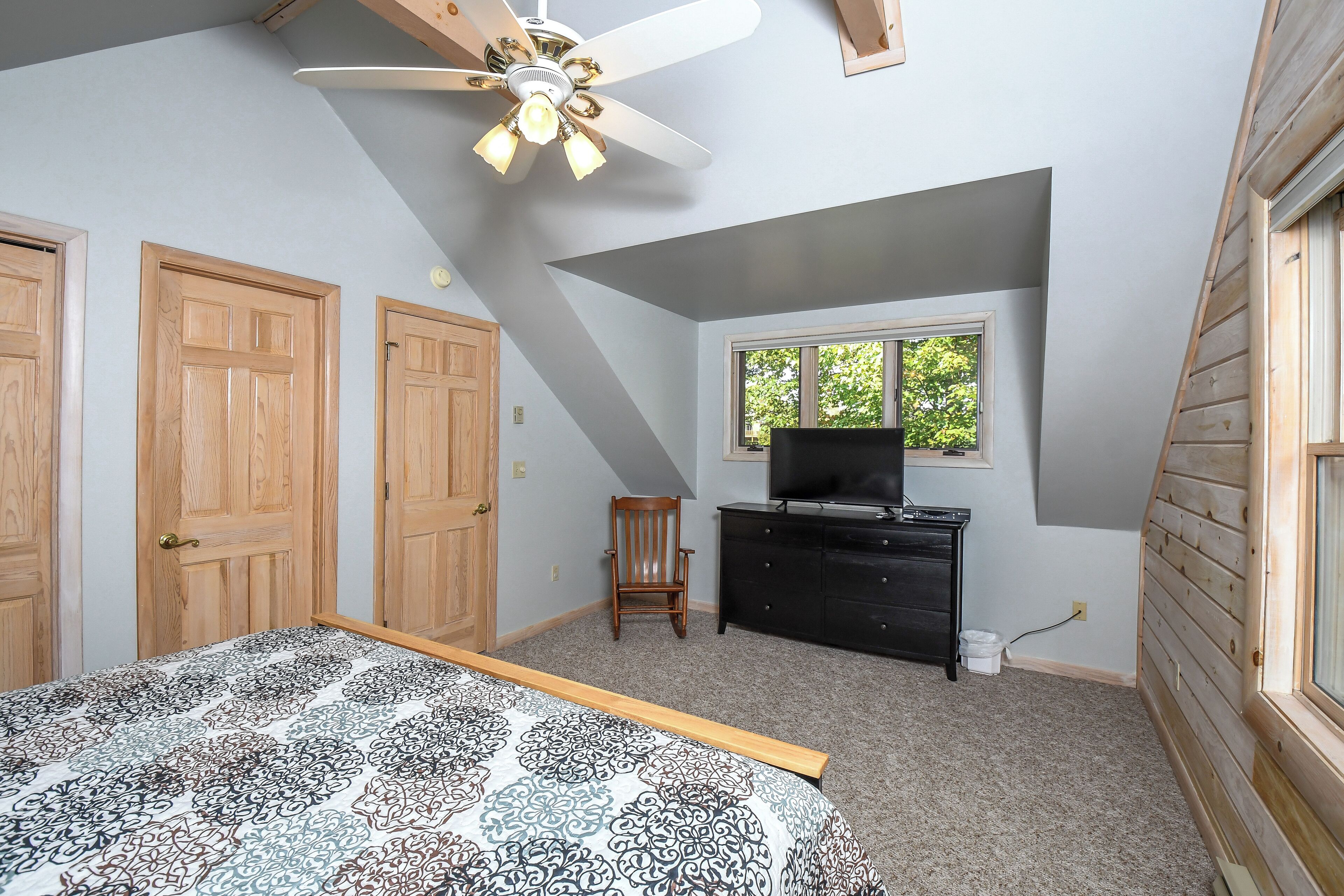 A bedroom with a bed, a ceiling fan, a dresser, a chair, and a window.