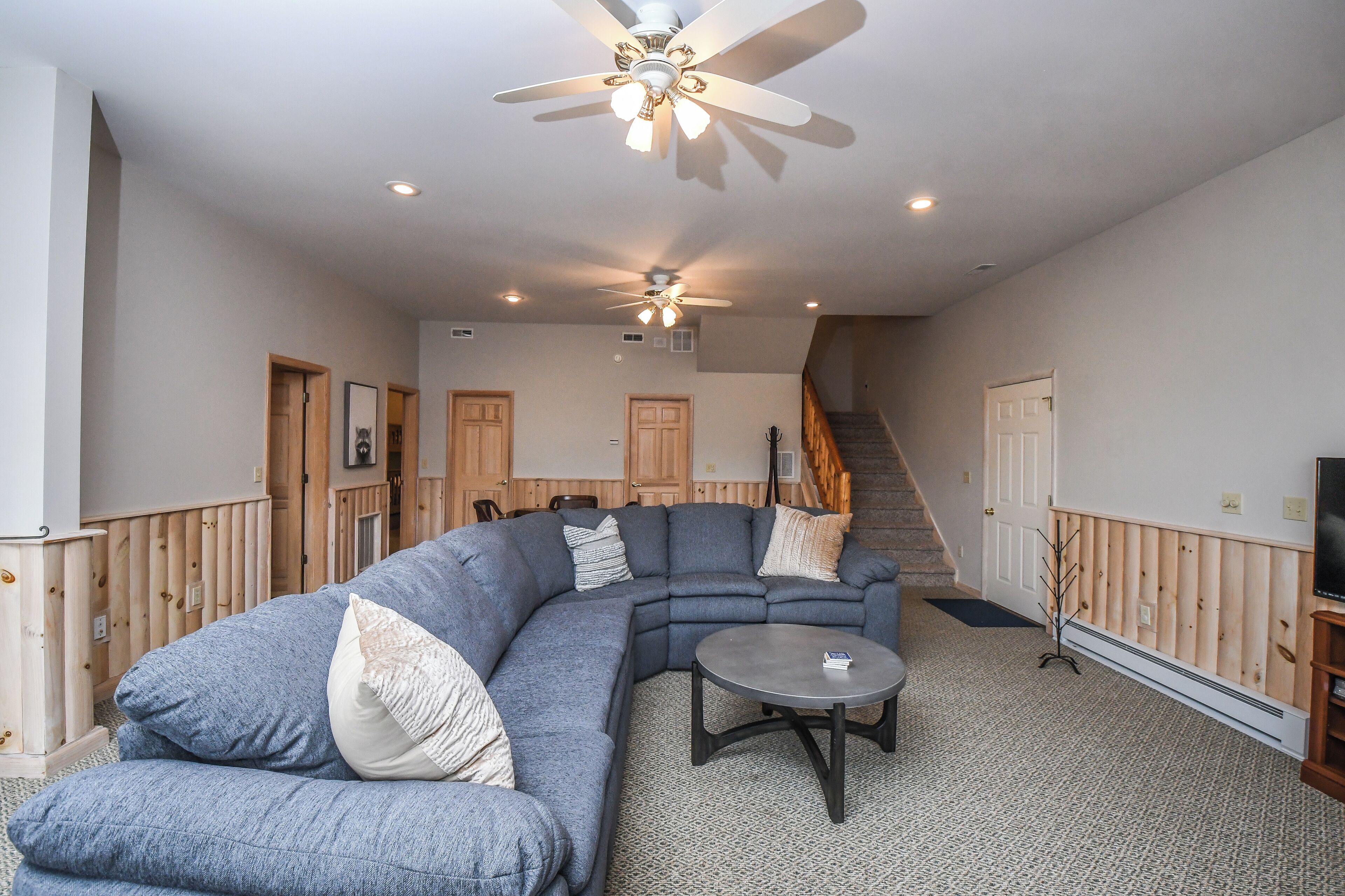 A living room with a large L-shaped sectional sofa, a round coffee table, and a ceiling fan.
