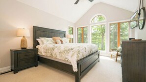 Quarto com uma cama grande, mesa de cabeceira, cômoda e ventilador de teto.