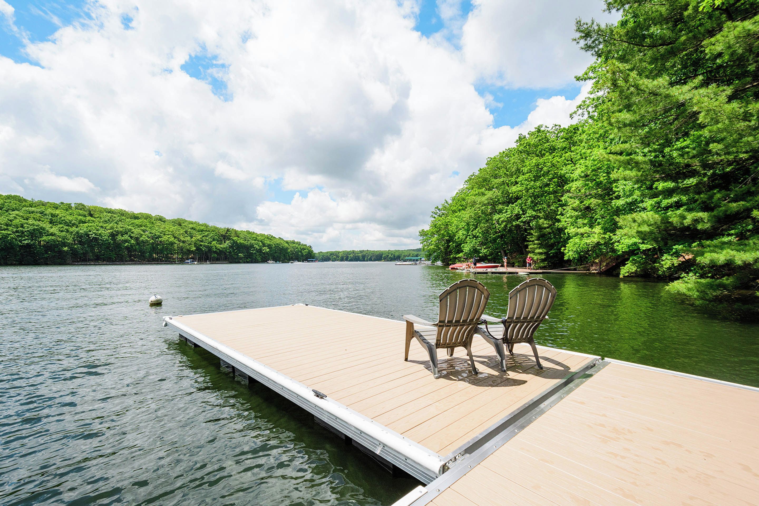 A wooden dock extending into a calm lake, surrounded by lush greenery.