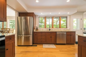 A modern kitchen with wooden cabinets, stainless steel appliances, and large windows. - Alpine Cove by Taylor Made Deep Creek (Swanton)