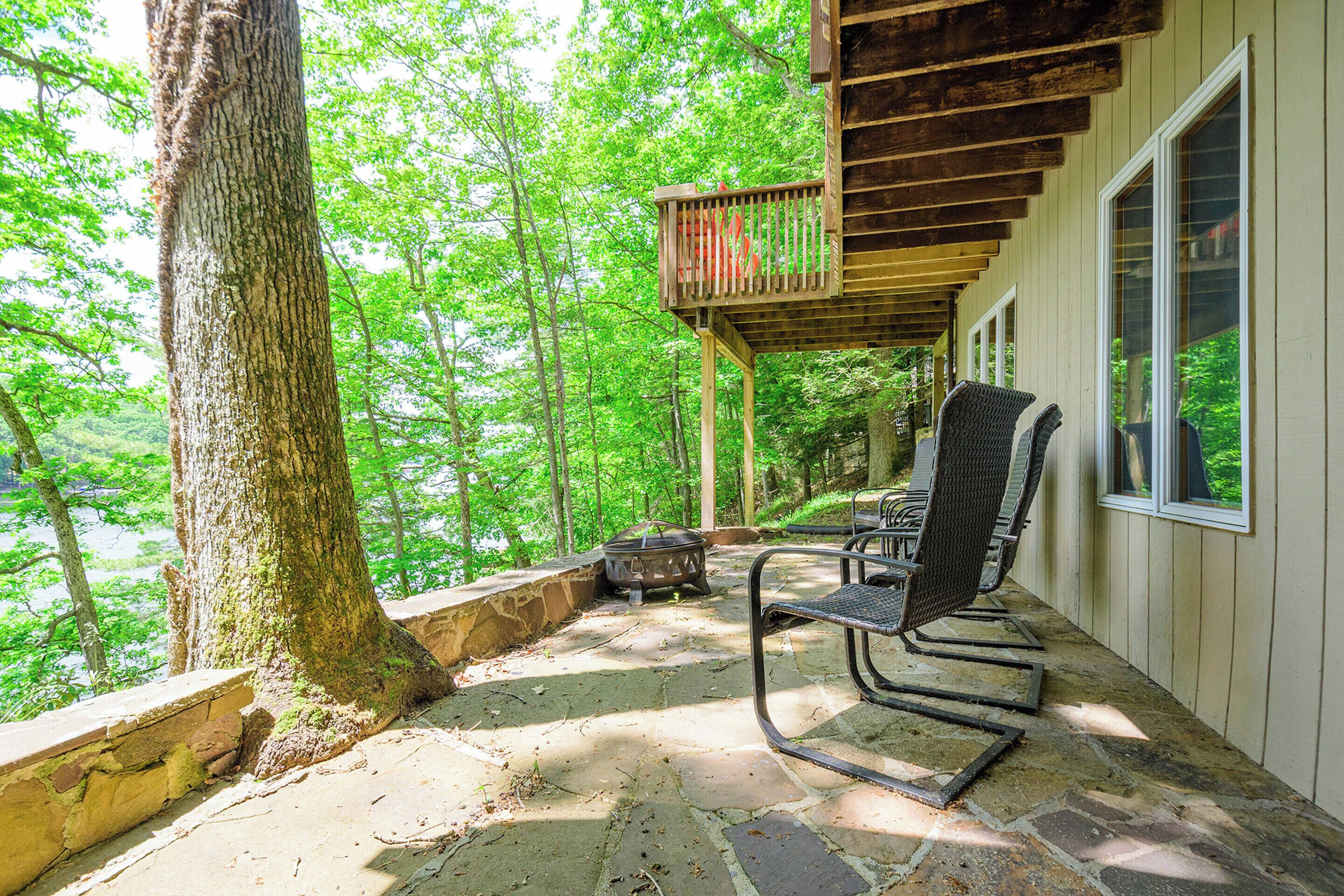 A covered outdoor seating area with stone flooring, surrounded by trees, and overlooking a forested area.