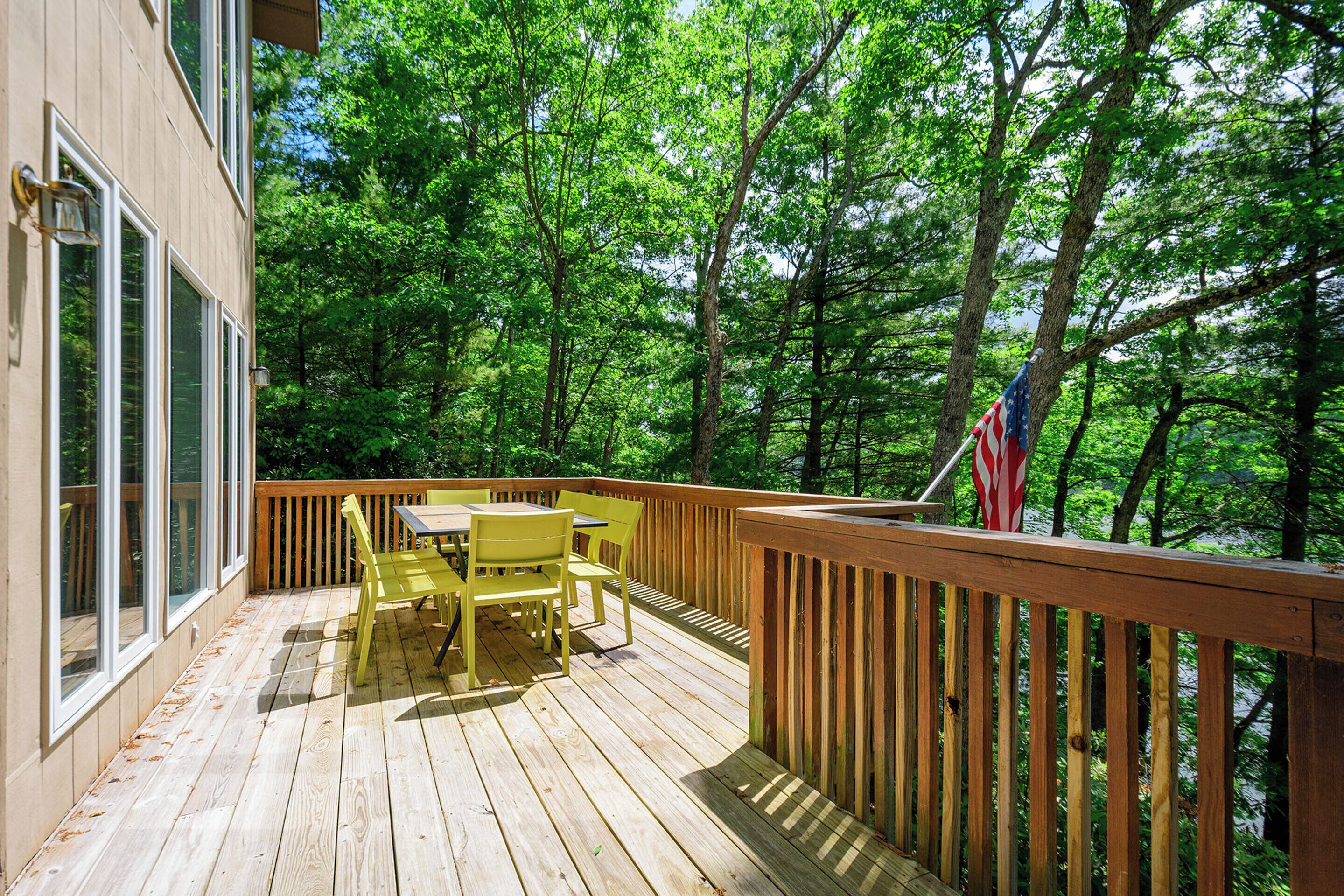 A wooden deck with yellow chairs and a table, surrounded by trees.