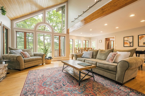 A spacious living room with large windows, a wooden ceiling, and a cozy seating area with two sofas and a coffee table. - Alpine Cove by Taylor Made Deep Creek (Swanton)