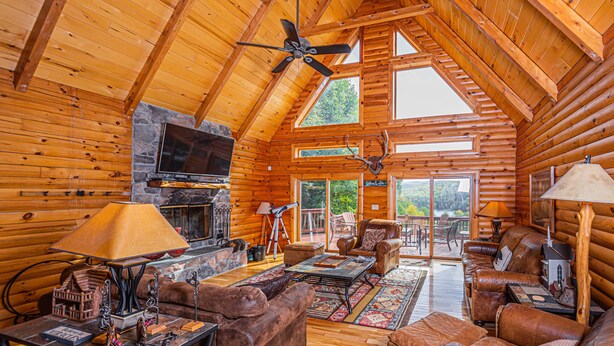 L’intérieur d’une cabane en rondins, avec un plafond en bois, une cheminée, des meubles en cuir et un téléviseur.