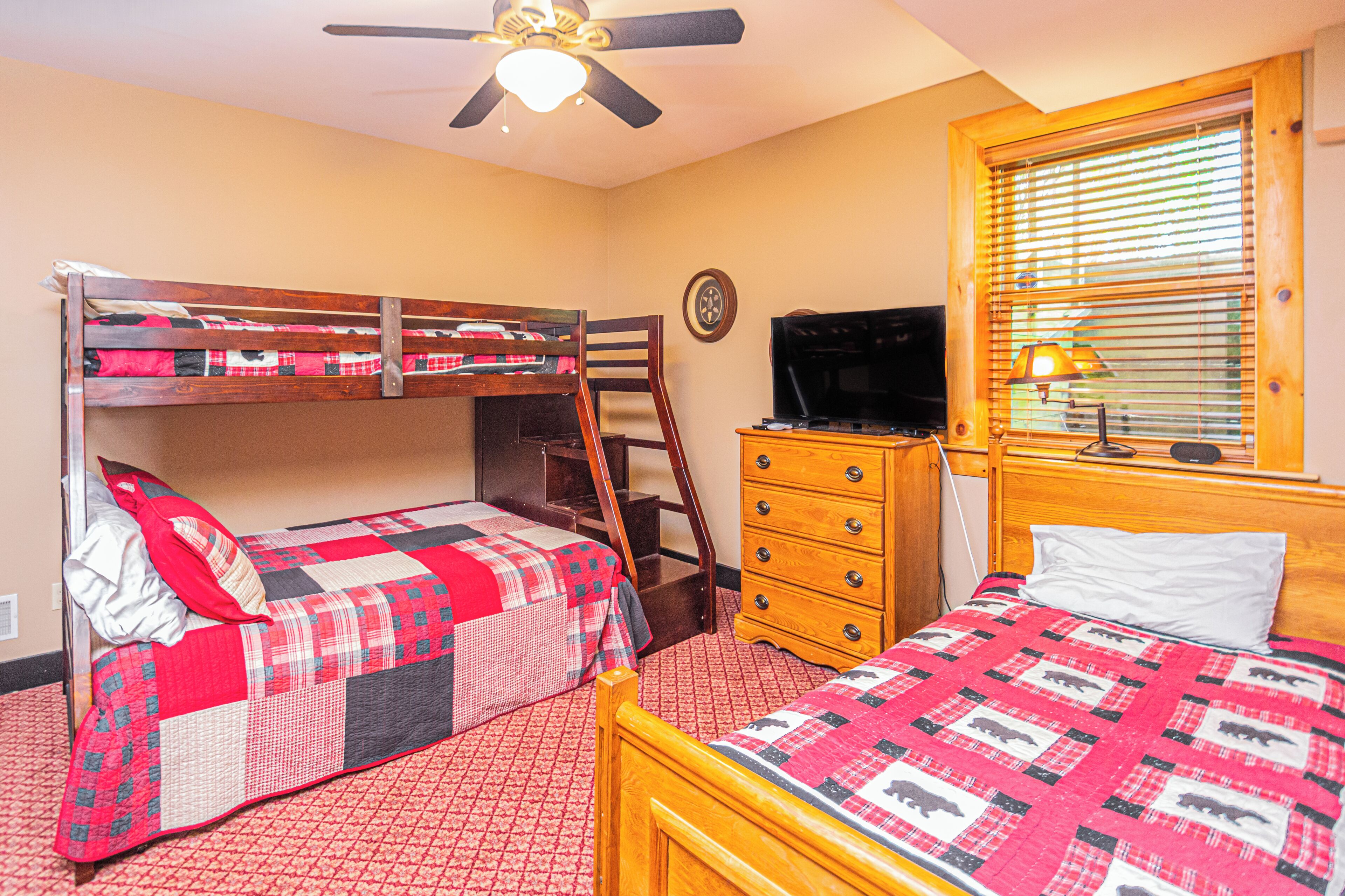 A room with bunk beds, a wooden dresser, a television, and a window with blinds.