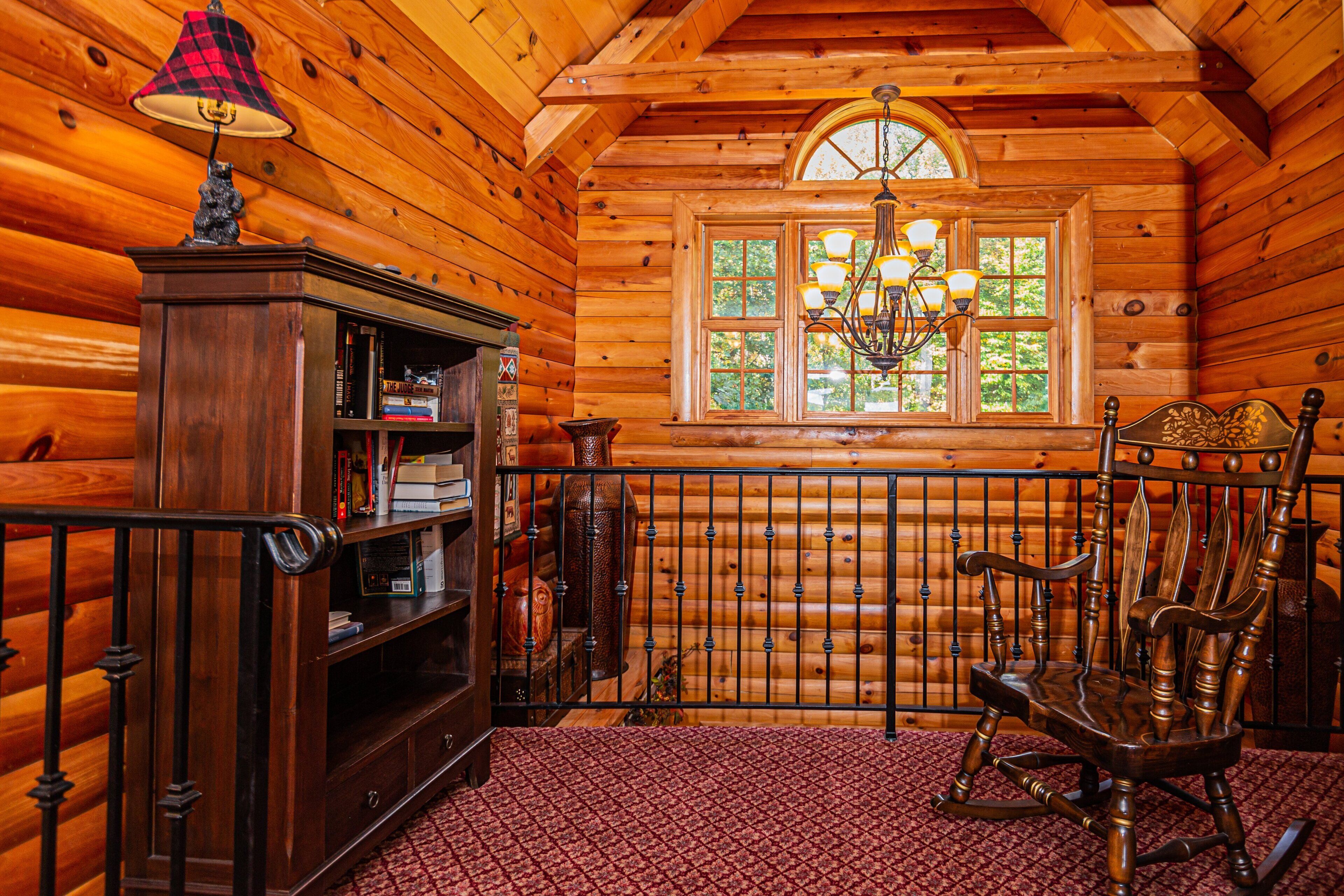 A log cabin interior with a rocking chair, a bookshelf, and a chandelier.