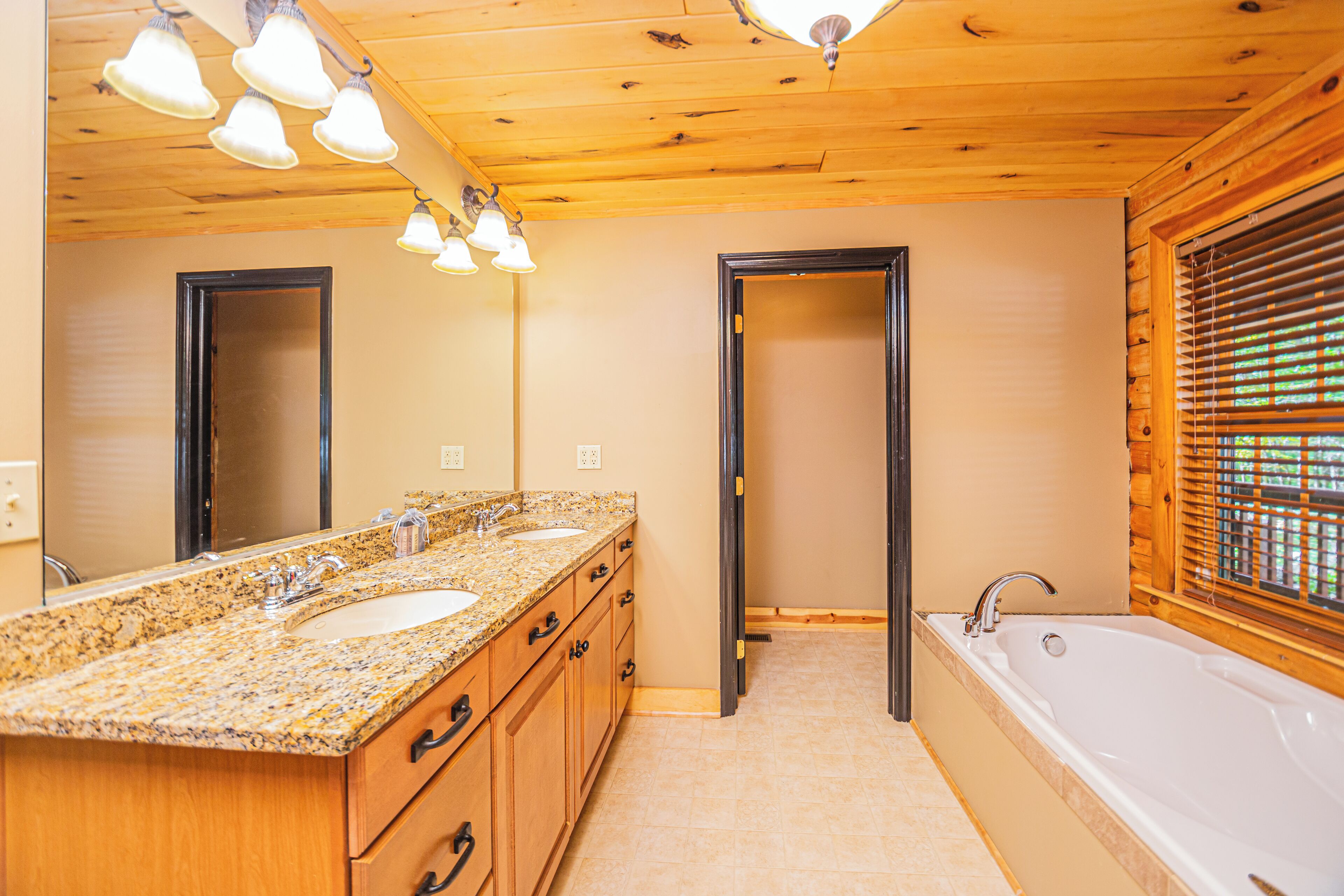 A bathroom with a granite countertop, two sinks, a bathtub, wooden cabinets, and a mirror.