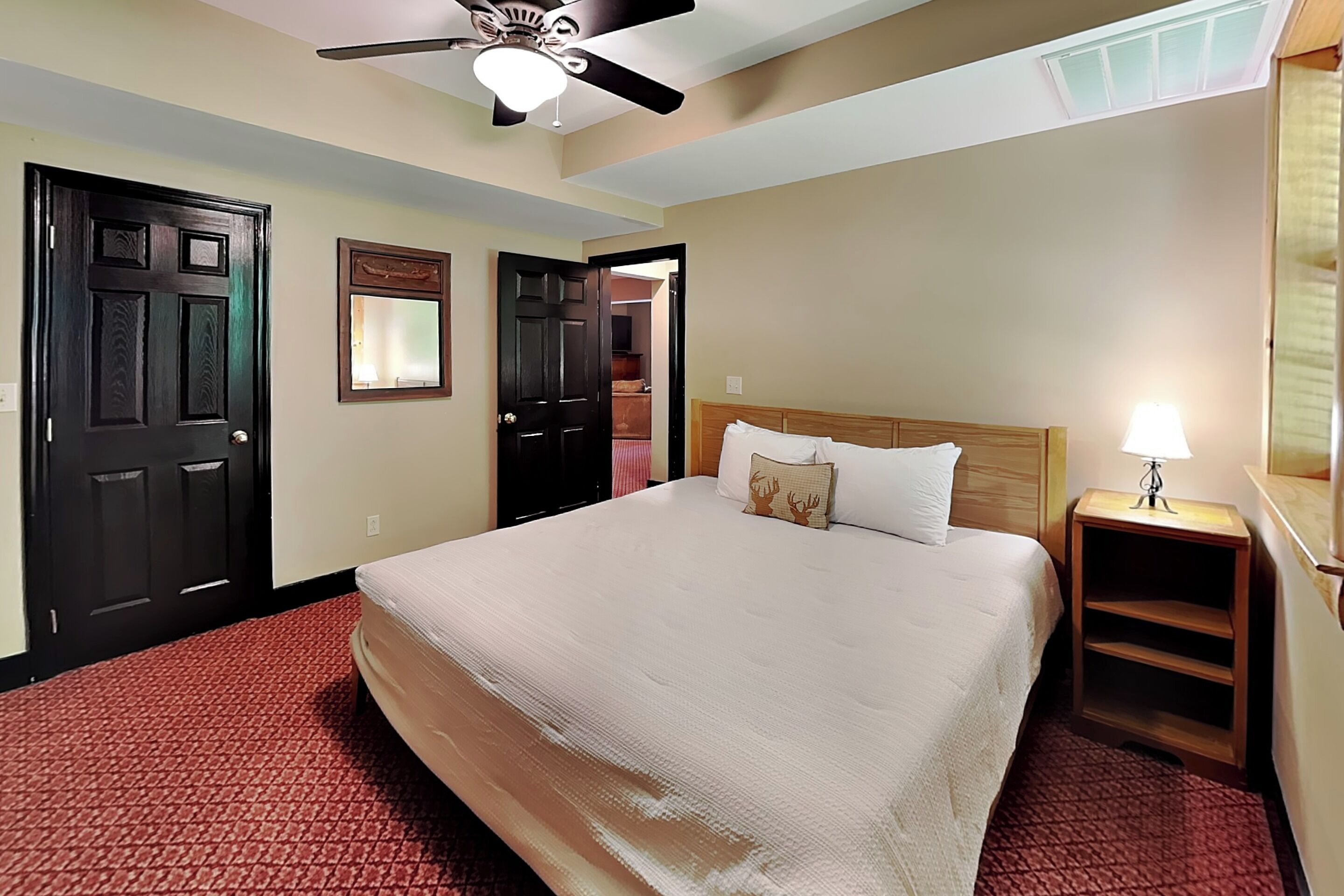 A hotel room with a bed, a nightstand, a ceiling fan, and a door.