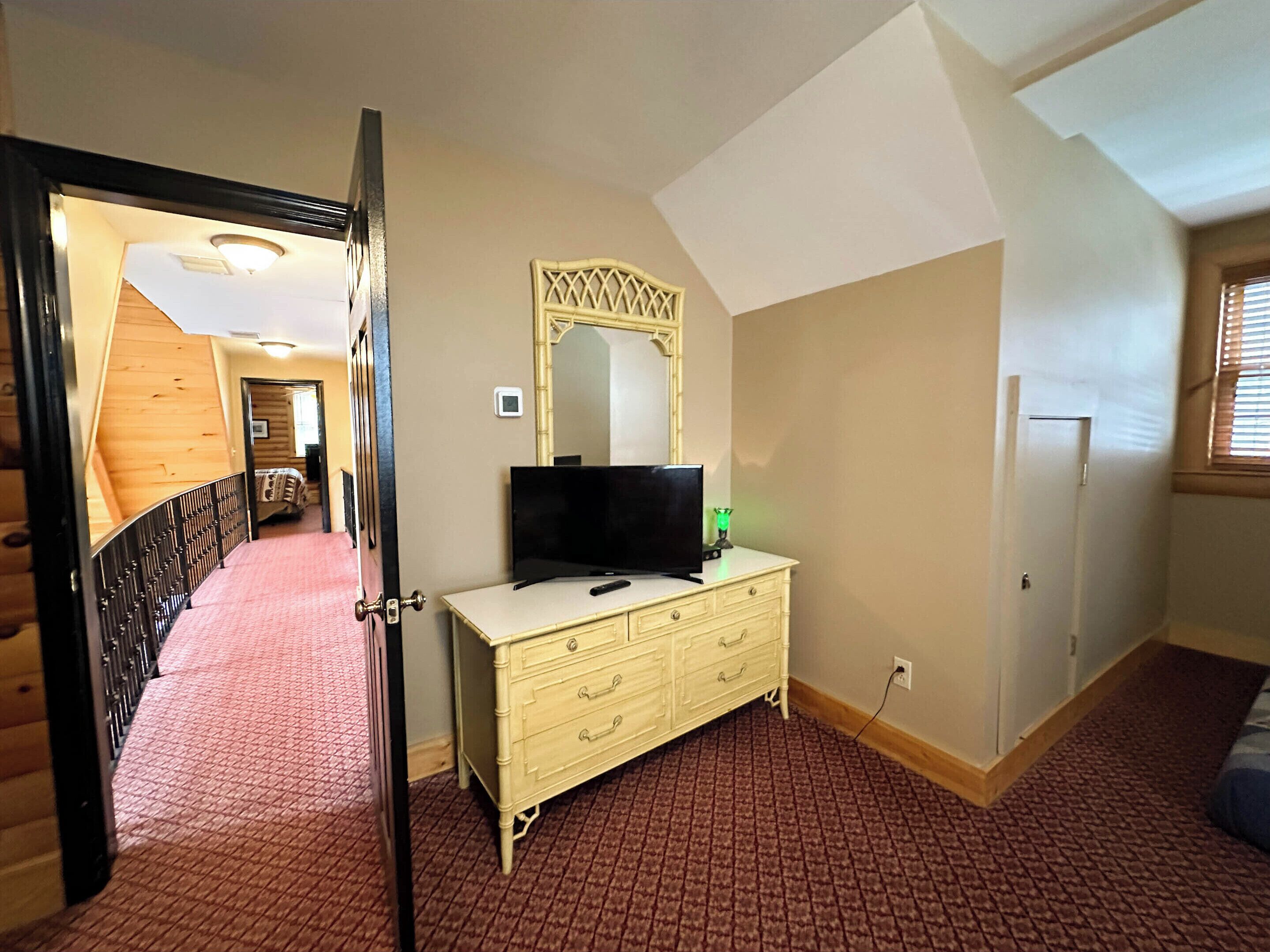 A bedroom with a bed, dresser, TV, and a mirror.