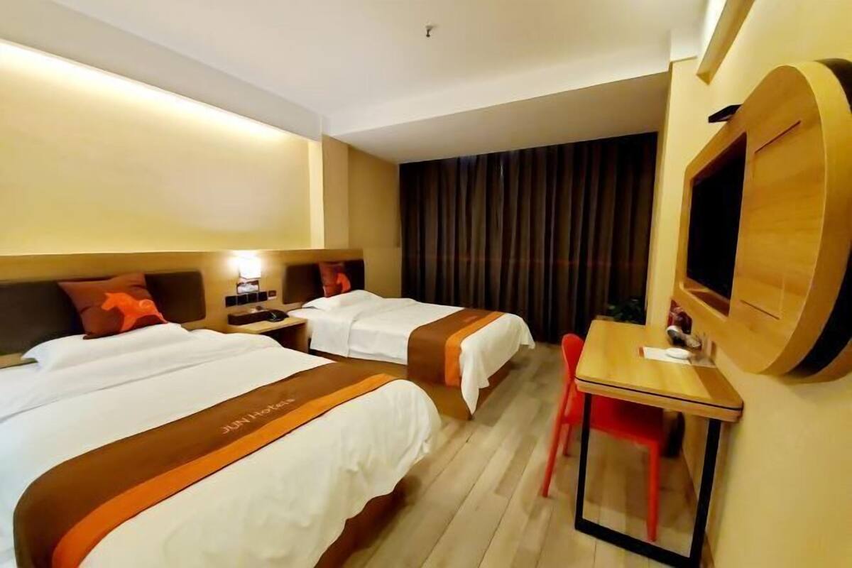 A hotel room with two beds, a desk, a chair, a TV, and a curtain.