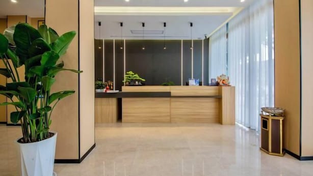 A modern reception area with a wooden reception desk, a large potted plant, and a view of the interior space. - Senlan Hotel (Zhongxiang Bus Station Branch) (Zhongxiang)