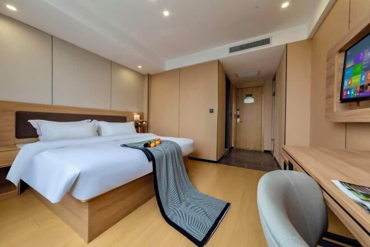A hotel room with a bed, a desk, a chair, a TV, and a door leading to a hallway.