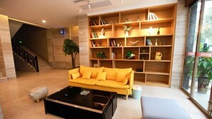 A modern lobby with a yellow sofa, a black coffee table, and a bookshelf filled with books and decorative items. - Senlan Hotel (Zhongxiang Bus Station Branch) (Zhongxiang)